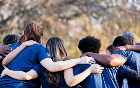 group of people wearing navy blue shirts with their arms around eachother facing away from the camera